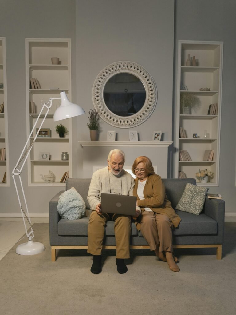 Senior couple sitting on sofa using laptop in cozy living room setting.